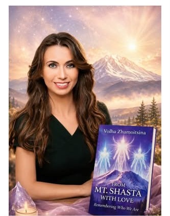A woman with long brown hair smiles while holding a book titled 'From Mt. Shasta with Love: Remembering Who We Are.' In the background, a mountain is visible under a mystical sky with ethereal lights.